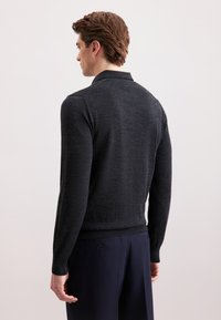 Dunkelgrauer Strickpullover mit langen Ärmeln und einem Kragen, ausgestattet mit einem gerippten Saum und Bündchen. Trägt dazu eine marineblaue Hose.