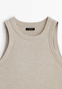 Haut en tricot beige côtelé sans manches avec encolure ronde, comportant une étiquette noire à l'intérieur du col indiquant « Massimo Dutti Made in China ».