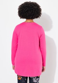 Langarmshirt in leuchtendem Pink mit rundem Halsausschnitt und lockerer Passform. Glattes, leichtes Material mit sichtbaren Nahtdetails.