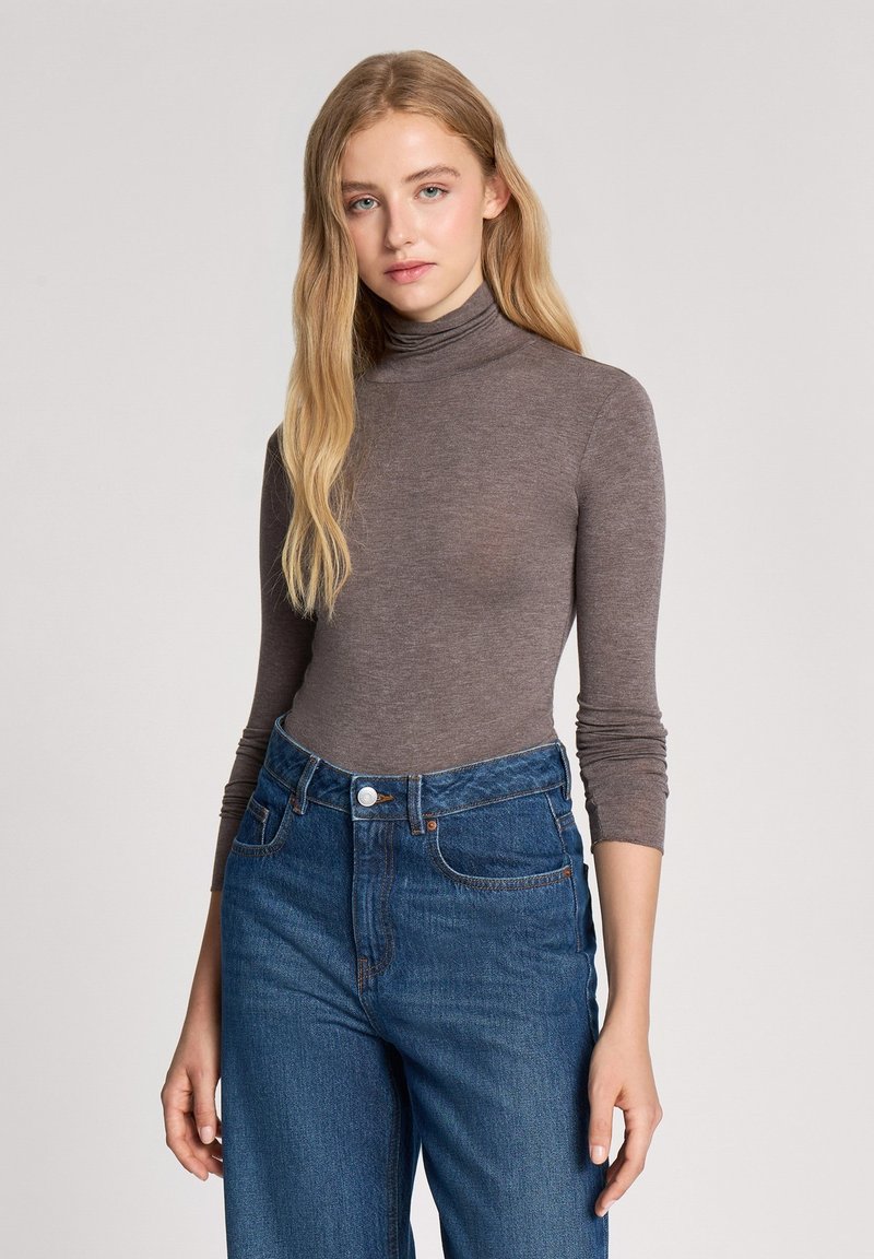 Maglione a collo alto marrone con maniche lunghe, dal design aderente. Abbinato a jeans in denim blu a vita alta con bottone e tasche.