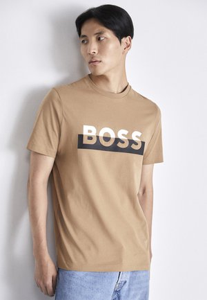 Beige T-Shirt mit kurzen Ärmeln aus Baumwolle und rundem Halsausschnitt. Mit einem auffälligen "BOSS"-Logo in Weiß auf einem schwarzen horizontalen Streifen über der Brust.