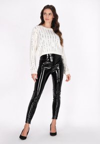 Weißer Strickpullover mit silbernen Streifen, kombiniert mit hochtaillierten schwarzen lackierten Kunstlederhosen. Schlichte schwarze Absatzschuhe runden das Outfit ab.