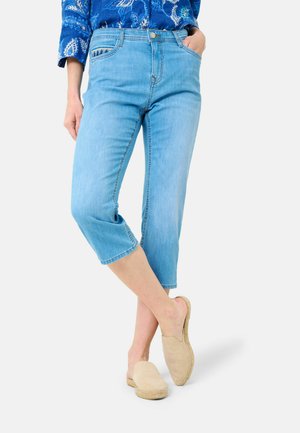 Jean cropped bleu clair en denim avec une coupe droite, affichant un design classique à cinq poches et un ourlet effiloché, accompagnés de chaussures beiges à enfiler.
