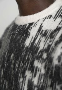 Sweter dzianinowy z czarno-białym abstrakcyjnym wzorem, okrągłym kołnierzem, miękką teksturą i lekko luźnym krojem.