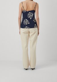 Námořnický květinový top bez rukávů s tenkými ramínky a volným střihem, kombinovaný s krémovými širokými kalhotami s minimalisticým designem a bez viditelného kování.