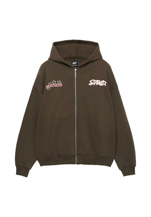 Brown zip-up hoodie with hood, featuring "MADRID" and "STND." in pink print. Includes two front pockets and ribbed cuffs. Soft fabric texture.
