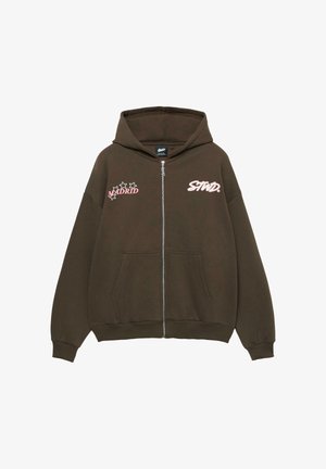 Brown zip-up hoodie with hood, featuring "MADRID" and "STND." in pink print. Includes two front pockets and ribbed cuffs. Soft fabric texture.