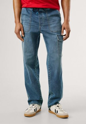 Pantalones de mezclilla azul claro con un ajuste holgado, que cuentan con dos bolsillos frontales y un bolsillo lateral tipo cargo. Combinados con zapatillas blancas.