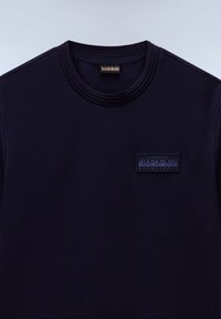 Camiseta de algodón azul marino con cuello redondo, que presenta un parche de logo texturizado en el pecho y detalles de costuras en contraste.