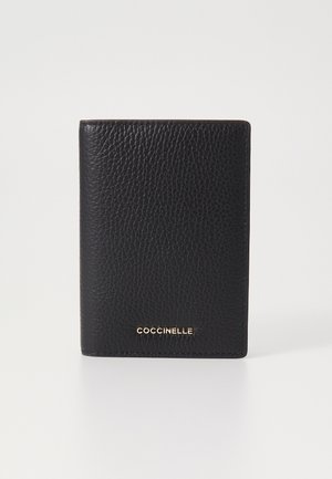 Carteira de couro preta com um acabamento texturizado. Apresenta um logo dourado na parte inferior e tem uma forma retangular. Bordas suaves e design minimalista.