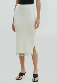 Crèmekleurige midirok van soepel materiaal, met een hoge split en een versierde franjes onderkant. Gecombineerd met zwart open hak sandaaltjes.