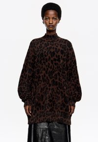 Suéter de pullover con estampado de leopardo marrón, con un cuello alto, mangas largas y un tejido suave y texturizado. Combinado con una falda de cuero negra.