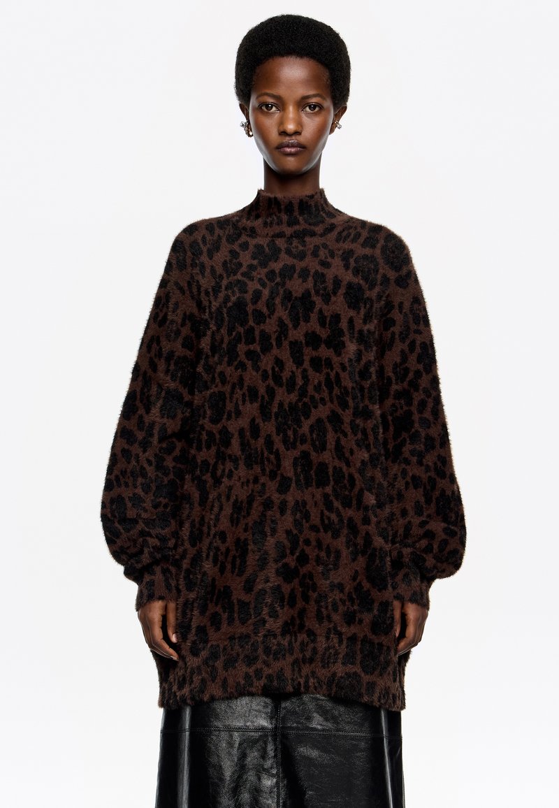 Suéter de pullover con estampado de leopardo marrón, con un cuello alto, mangas largas y un tejido suave y texturizado. Combinado con una falda de cuero negra.