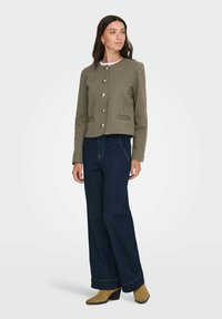 Houndstooth-patterned jacket in brown and beige with gold buttons, paired with dark blue wide-leg jeans and tan ankle boots.