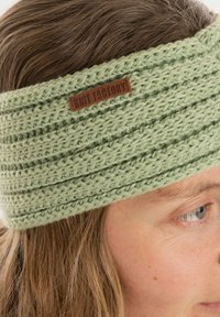 Miętowozielona opaska na głowę z dzianiny o prążkowanym wzorze, z brązową skórzaną metką oznaczoną "Knit Factory". Miękka faktura, szeroki krój.