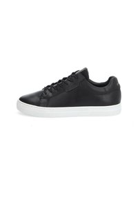 Baskets en cuir noir avec semelle en caoutchouc blanche, présentant un bout arrondi, un système de laçage et un design minimaliste. Des accents incluent un logo discret.