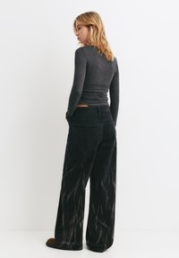 Sorte vide ben jeans med et falmet mønster, parret med en tætsiddende grå langærmet trøje. Stoffet ser blødt ud med en glat tekstur.