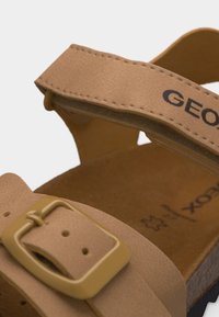 Κλείσιμο των λουριών μιας ταμπαριζέ σάνδαλας με πλαστική αγκράφα και ορατό κείμενο μάρκας στο λουρί στον αστράγαλο και στο πέλμα.