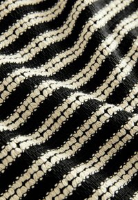 Schwarzer und cremefarbener gestreifter Stoff mit einer strukturierten Webart, gewellten Mustern und offenen Strickakzenten, die abwechselnd einfarbige und gemusterte Streifen zeigen.