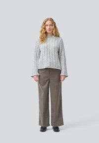 Maglione grigio chiaro a trecce con maniche ampie, abbinato a pantaloni marroni a vita alta, con taglio dritto e scarpe nere.