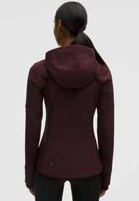 Vinröd huva-jacka med en åtsittande design, elastiskt material och en dragkedjeficka på baksidan. Har subtila texturerade detaljer.