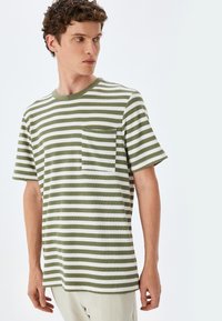 Randig T-shirt i olivgrön och vit. Korta ärmar, rund hals och en framficka. Mjuk textur med horisontella ränder.