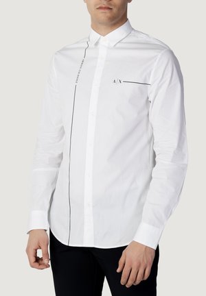 Homme portant une chemise blanche à manches longues avec des lignes noires verticales et horizontales et des logos Armani Exchange.