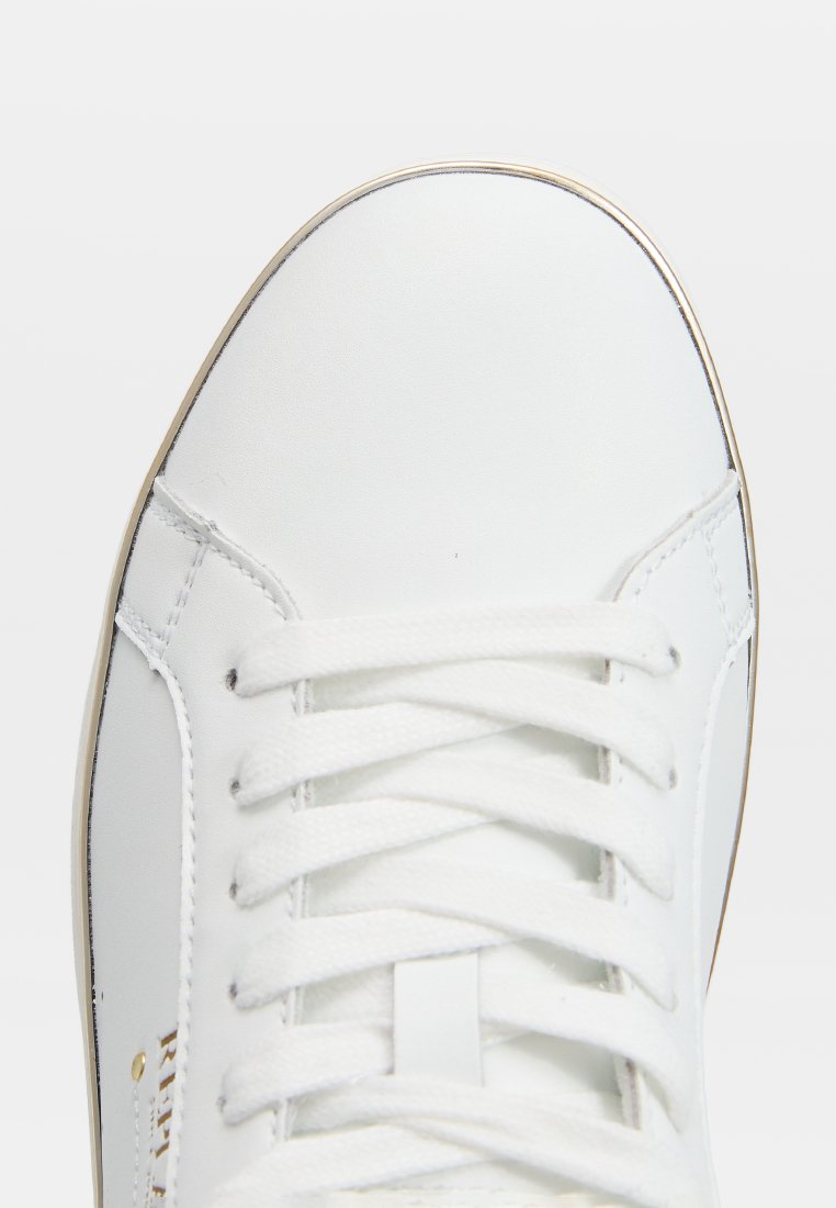 Bouton de sneaker en cuir blanc avec des lacets blancs et des coutures visibles sur un fond blanc uni.