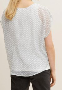 Blusa bianca con un motivo a onda testurizzato, maniche corte e scollatura rotonda. Tessuto morbido e leggero con una finitura leggermente trasparente.