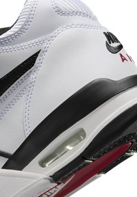 Chaussure de sport blanche avec des accents noirs, empeigne synthétique texturée, unité de amorti d'air visible et semelle en caoutchouc avec des détails rouges.