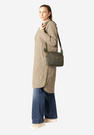 Quiltet beige jersey-kjole med lange ærmer, knapdetaljer, parret med en grøn crossbody taske og brede denimbukser. Tekstur og afslappet pasform.