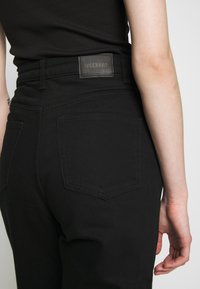 Jeans pretos de cintura alta com um patch de couro rotulado "WEEKDAY", bolsos traseiros e uma textura de denim suave.