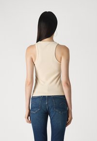 Top din bumbac bej cu dungi, cu bretele late, design ajustat și decolteu rotund, asortat cu blugi negri bleu cu buzunare cusute la spate.