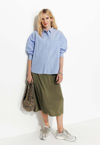 Chemise bleu clair à boutonnières avec des manches bouffantes, jupe midi vert olive, baskets argentées et sac fourre-tout imprimé léopard.