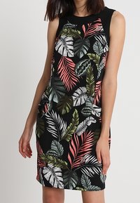 Sleeveless black dress featuring vibrant tropical leaf patterns in green, pink, and white. Soft fabric with a fitted style and round neckline.