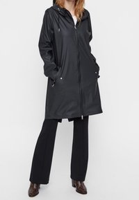 Manteau de pluie noir imperméable avec capuche, fermeture éclair à l'avant et deux poches latérales. Caractérisé par une texture lisse et un cordon de serrage ajustable.