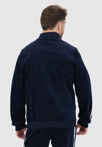 Marineblauwe corduroy jas met een geribbelde kraag, lange mouwen en geribbelde manchetten. Kenmerkt zich door de textuurstof en een rechte snit.