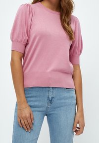 Ljusrosa stickad tröja med korta puffärmar och ribbade manschetter, kombinerad med ljusblå jeans. Slät textur, avslappnad design.