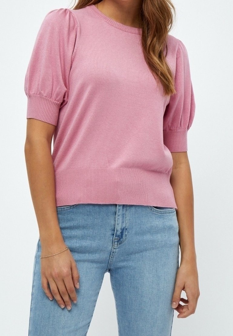Ljusrosa stickad tröja med korta puffärmar och ribbade manschetter, kombinerad med ljusblå jeans. Slät textur, avslappnad design.