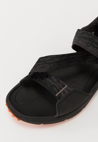 Schwarze Sandalen mit strukturierten schwarzen Riemen, orangefarbigen Akzenten an der Sohle, ausgestattet mit einer gepolsterten Fußbett und einem ergonomischen Design.