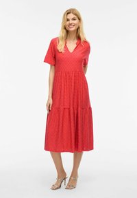 Robe rouge à manches courtes avec décolleté en V, découpes brodées, jupe à volants et coupe décontractée. Le matériau semble léger et texturé.