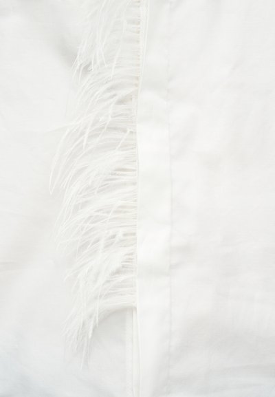 Κοντινό πλάνο λευκού υφάσματος με μια σειρά από λεπτά, απαλά λευκά φτερά προσαρτημένα κατά μήκος μιας κεντρικής ραφής.