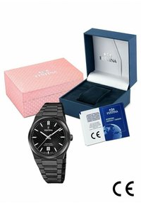 Montre en acier inoxydable noir avec cadran noir texturé et accents argentés. Comprend une boîte rose, une carte de garantie bleue et un coussin de présentation.