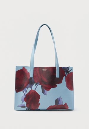 Blue tote bag with red rose print, features two long handles, textured surface, and brand logo in silver at the top center.