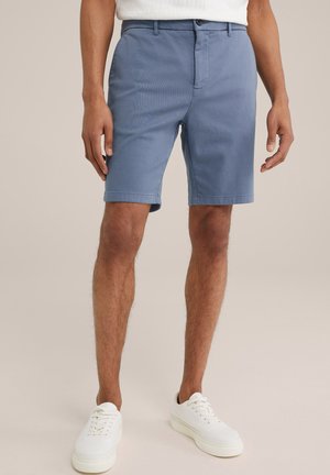 Shorts bleus en mélange de coton, avec une taille plate, des poches latérales et des ourlets roulés, associés à des baskets blanches. Texture lisse.