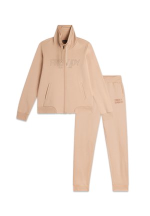 Giacca beige con zip e collo alto, dotata di due tasche, abbinata a pantaloni della tuta coordinati. Entrambi presentano "FREDDY TRAINING" ricamato in beige.
