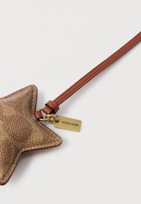 Hnedé kožené vrecko v tvare hviezdy s reliéfnym vzorom, bordovým vnútorným prešívaním a hnedým koženým remienkom. Pripojená zlatá visačka s nápisom „COACH“.