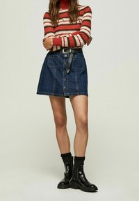 Denimkjol med framslutna knappar, två framfickor och ett svart bälte. Tillsammans med en randig stickad tröja i röd och gräddfärg och svarta ankelstövlar.