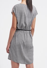 Kortärmad klänning i svart och vitt, med en diamantmönster, cinched midja med bälte, och något utsvängd kjol.