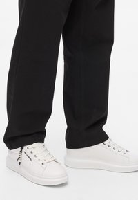 Valged tennisekingad sileda nahapinnaga, ümmargune varvas ja lame tald. Omavad paelu, brändimist külgedel ja musta aktsenti.